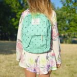 woman in white and multicolored floral long-sleeved mini dress with green backpack